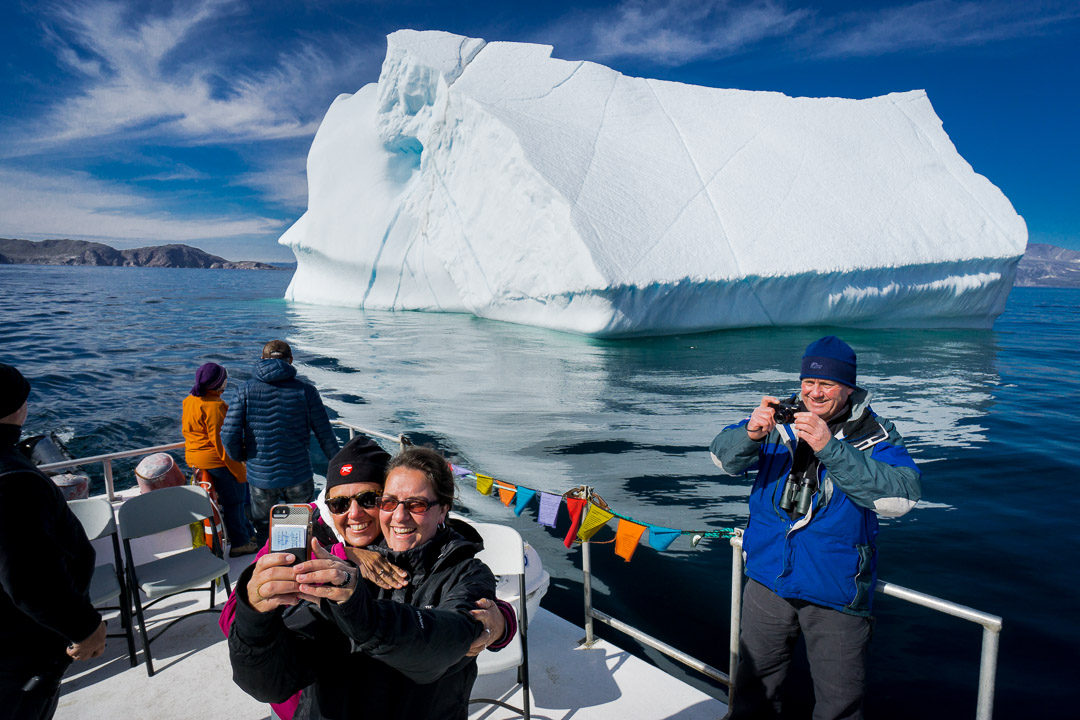 Iceberg from Greenland floats past Big Island, and Liz Fleming and Janice Goudie take a selfie aboard the Inuttatik passenger boat, Torngat Mountains National Park , Northern Labrador Mountains, (Newfoundland and Labrador), Canada