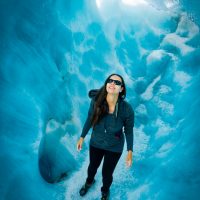 An adventure tourist revels in the coolness of a melted out crevasse, Alpine Guides guided helihike on the Tasman glacier, Aoraki/Mt Cook National Park, New Zealand (client Elena Ferrari)