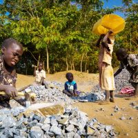 An impoverished family is employed to turn rocks into gravel the hard way -
