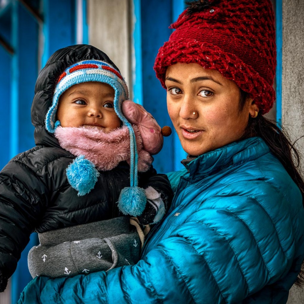 A mom and her child bundle up to keep warm after first snowfall in Lukla.